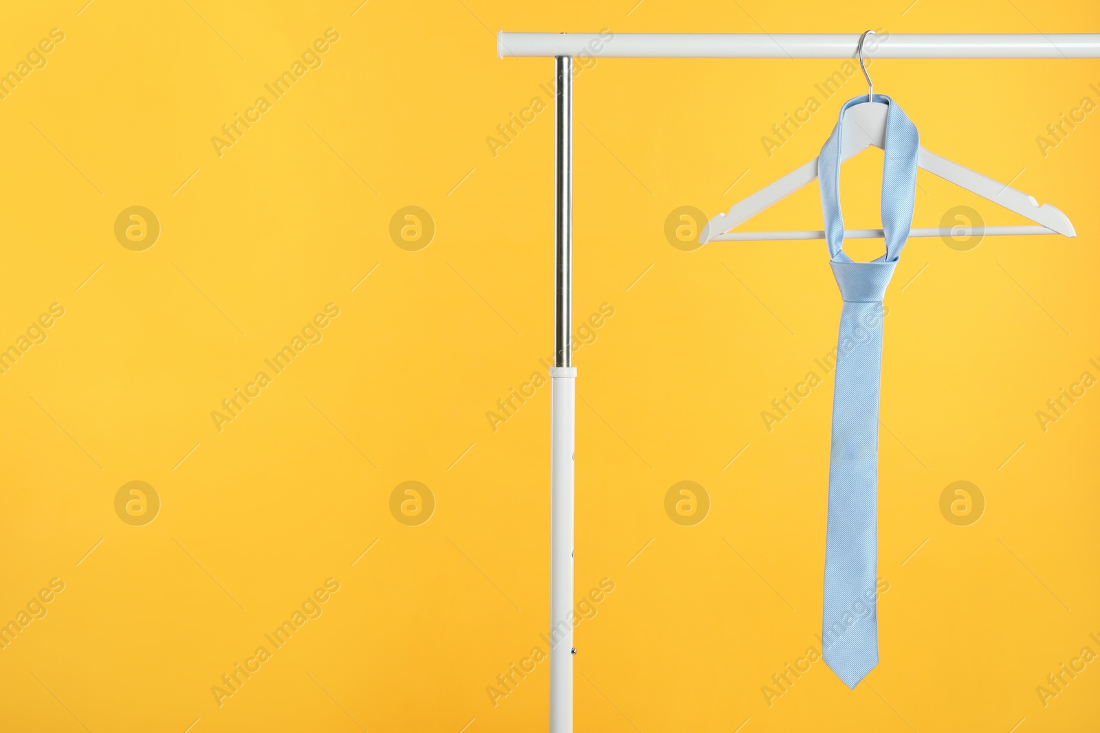 Photo of Hanger with light blue tie on rack against orange background. Space for text