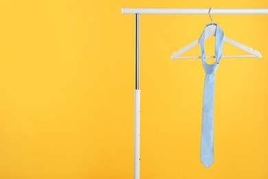 Photo of Hanger with light blue tie on rack against orange background. Space for text