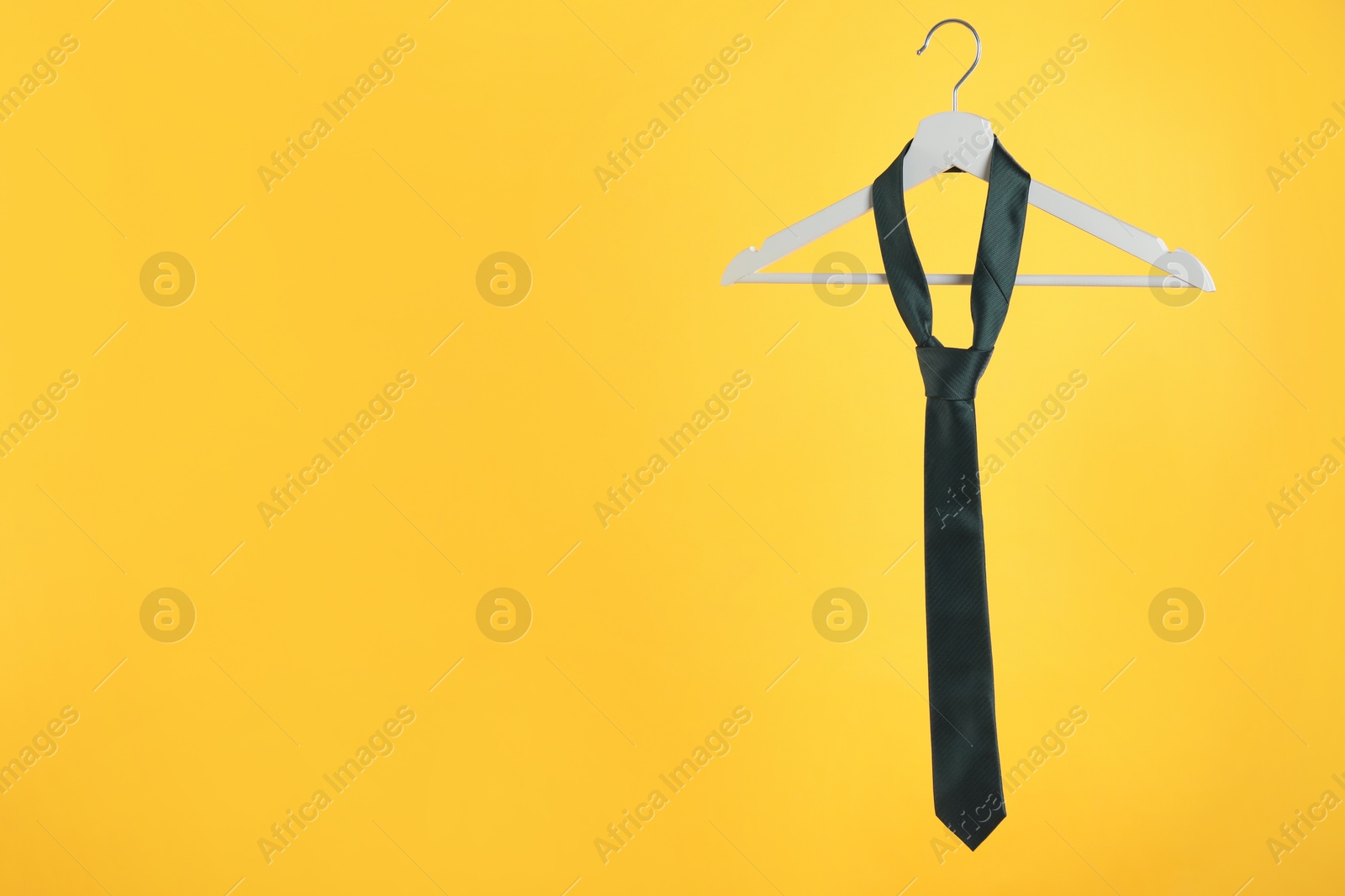 Photo of Hanger with black tie against orange background. Space for text