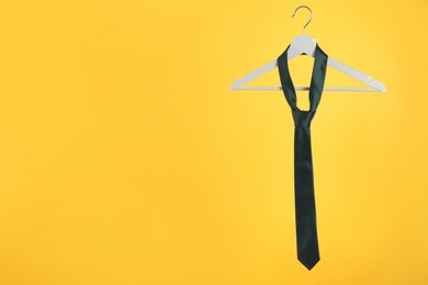 Hanger with black tie against orange background. Space for text