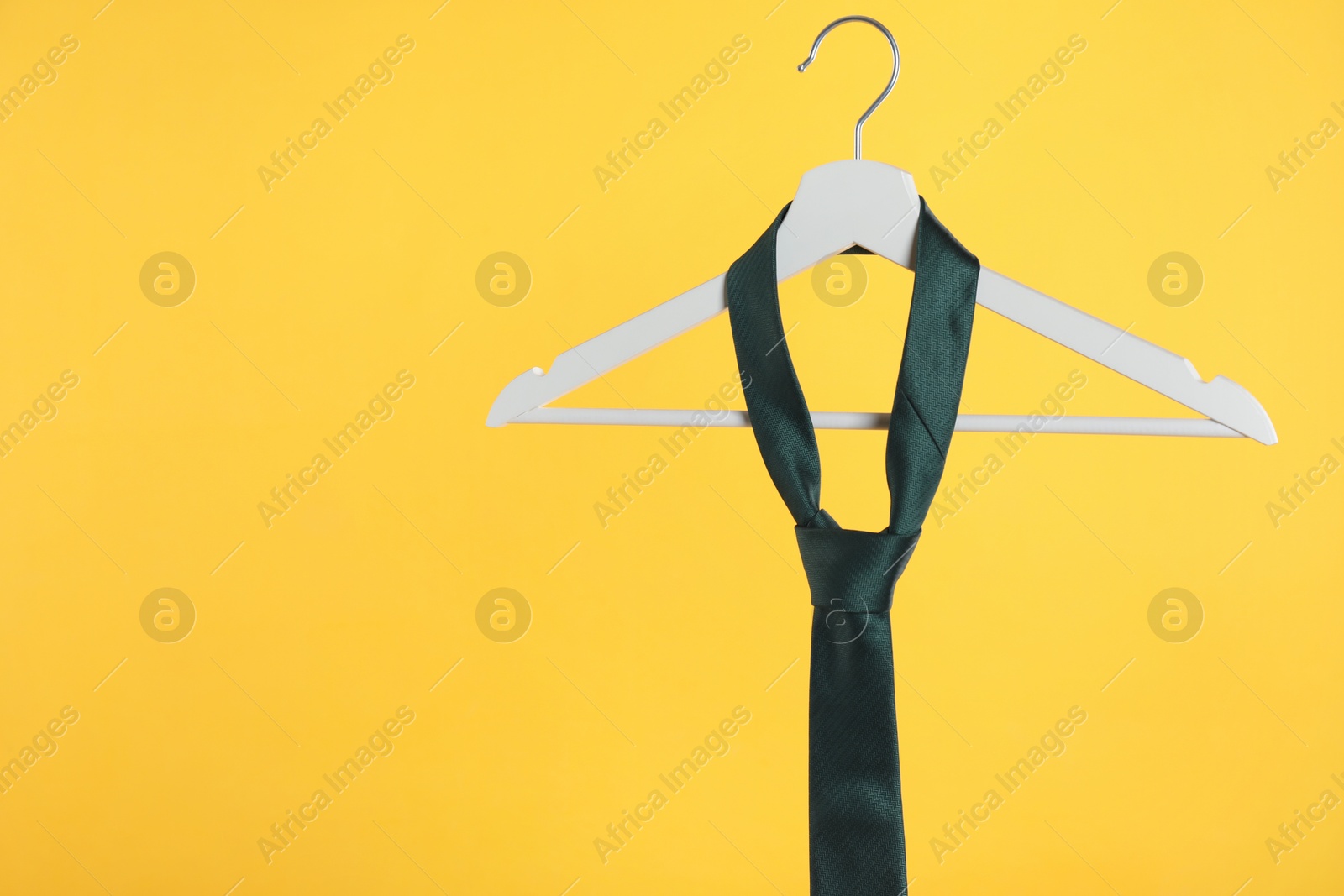 Photo of Hanger with black tie against orange background. Space for text