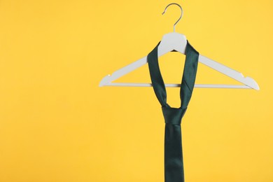 Hanger with black tie against orange background. Space for text