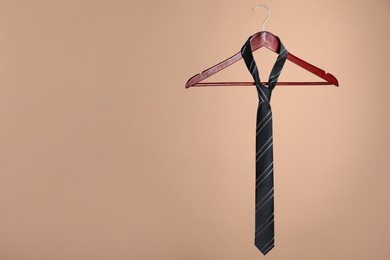 Photo of Hanger with black striped tie on light brown background. Space for text