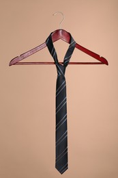 Photo of Hanger with black striped tie on light brown background