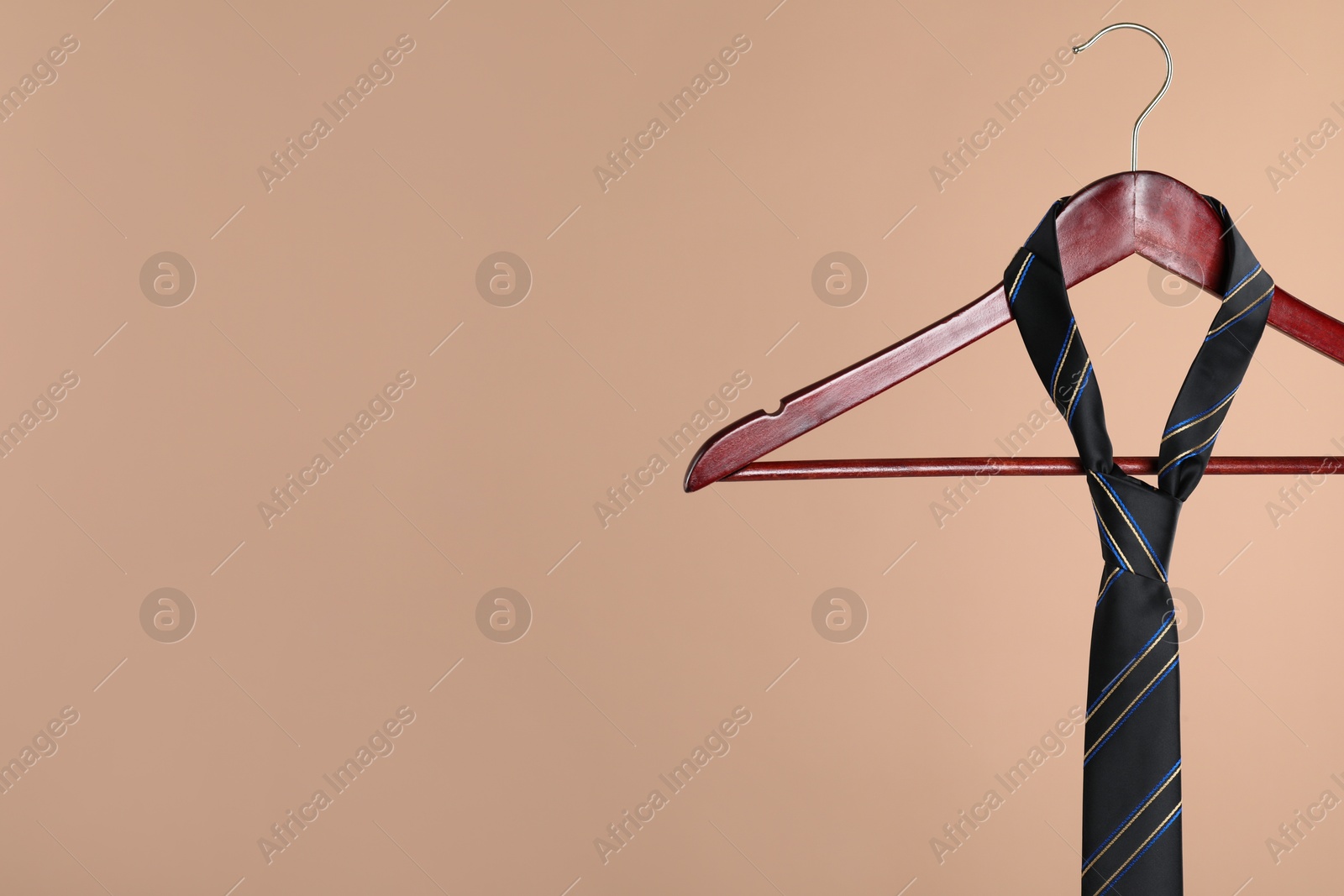 Photo of Hanger with black striped tie on light brown background. Space for text