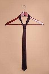 Photo of Hanger with silk tie on light brown background
