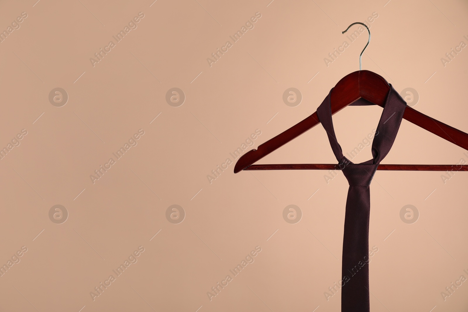 Photo of Hanger with silk tie on light brown background. Space for text
