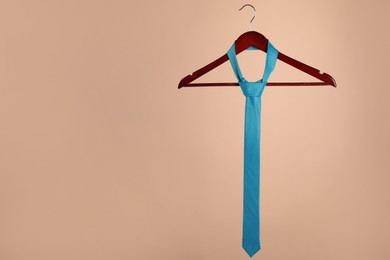 Photo of Hanger with turquoise tie on light brown background. Space for text