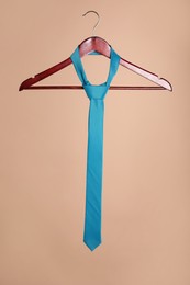 Photo of Hanger with turquoise tie on light brown background
