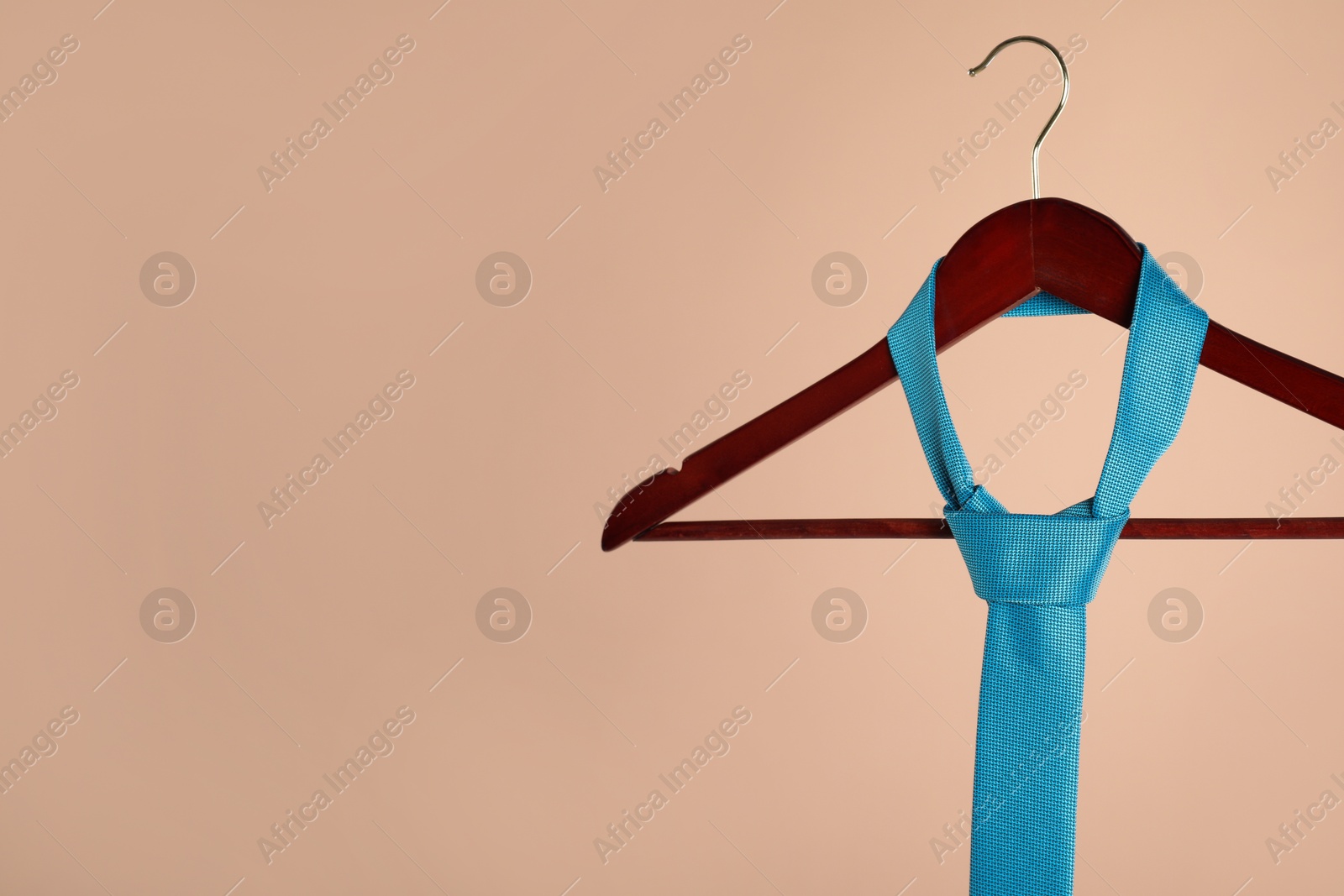 Photo of Hanger with turquoise tie on light brown background. Space for text