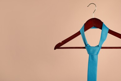 Hanger with turquoise tie on light brown background. Space for text