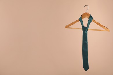 Photo of Hanger with teal tie on light brown background. Space for text