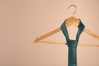 Photo of Hanger with teal tie on light brown background, closeup. Space for text
