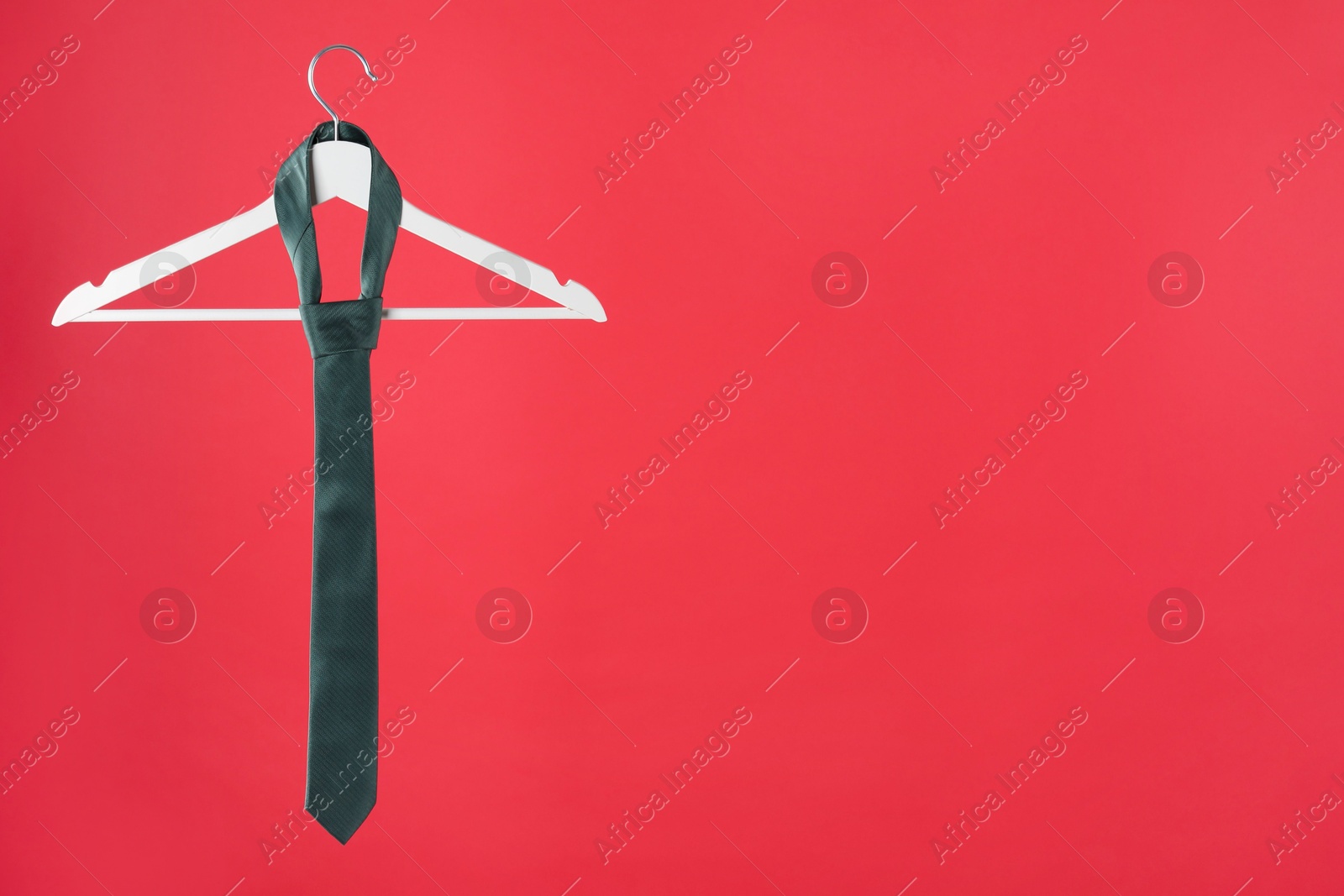 Photo of Hanger with teal tie on red background. Space for text