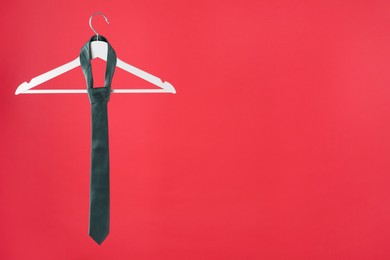 Hanger with teal tie on red background. Space for text