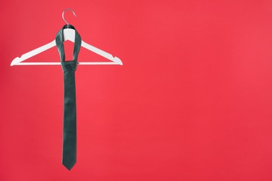 Photo of Hanger with teal tie on red background. Space for text