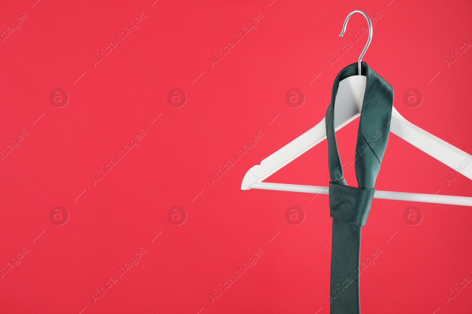 Photo of Hanger with teal tie on red background. Space for text