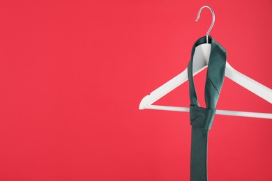 Photo of Hanger with teal tie on red background. Space for text