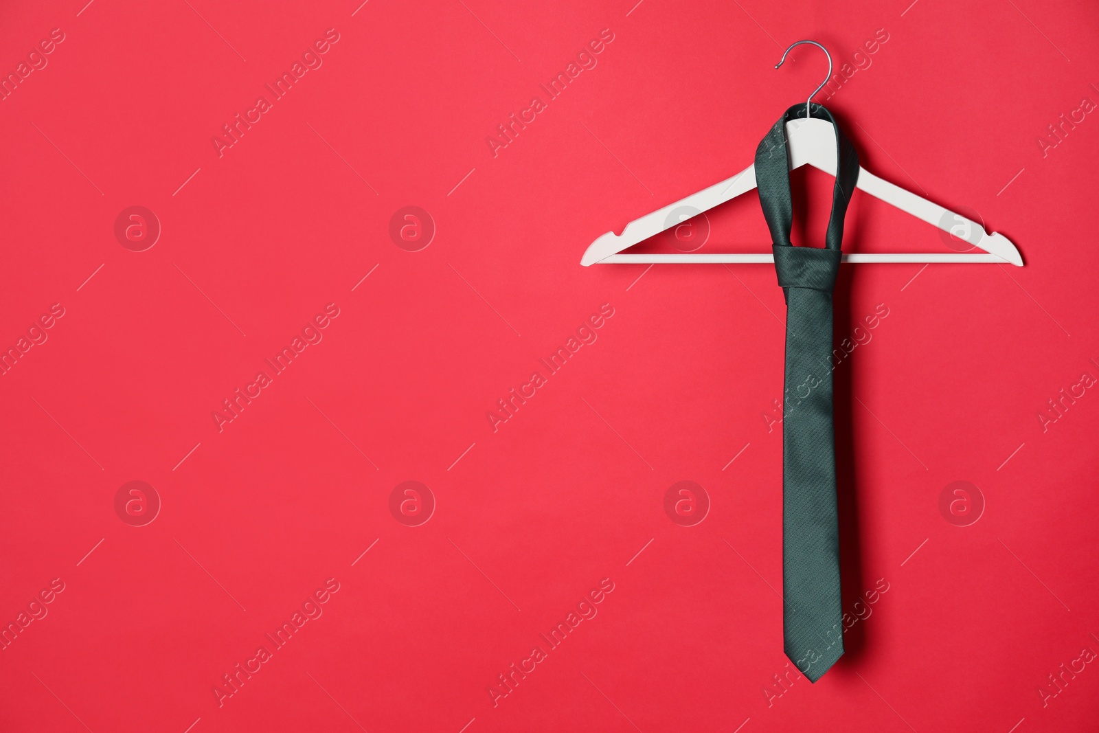 Photo of Hanger with black tie on red background. Space for text