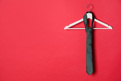 Hanger with black tie on red background. Space for text