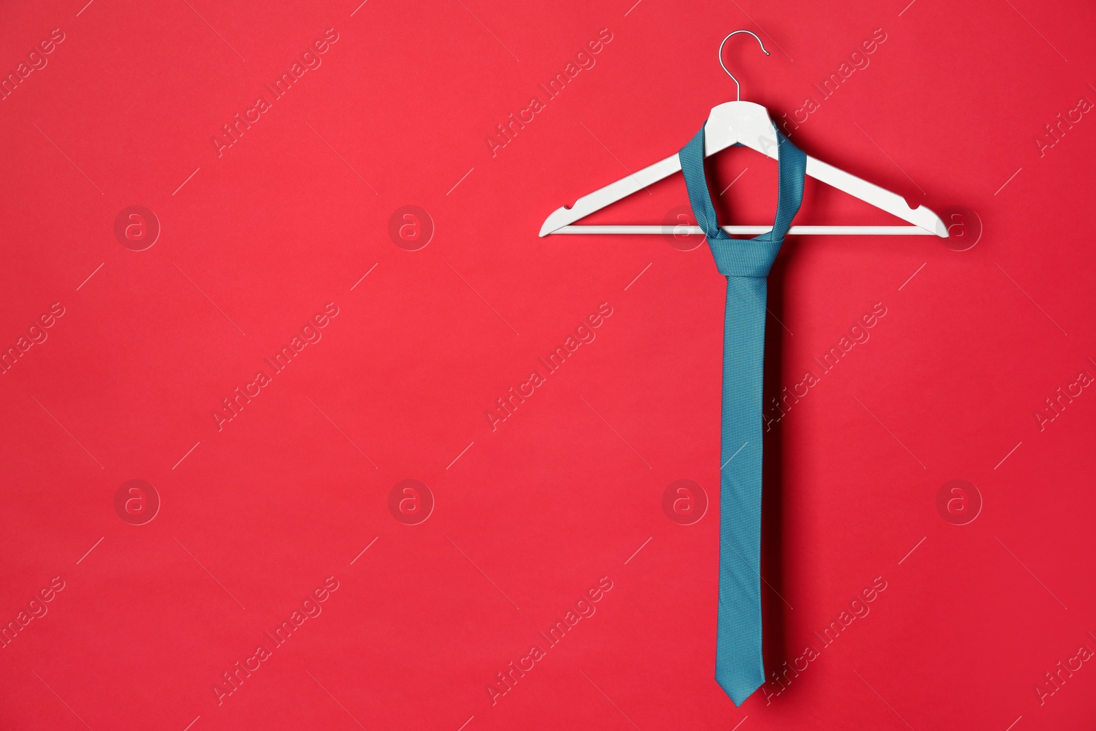 Photo of Hanger with dark turquoise tie on red background. Space for text