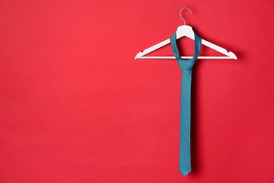 Hanger with dark turquoise tie on red background. Space for text