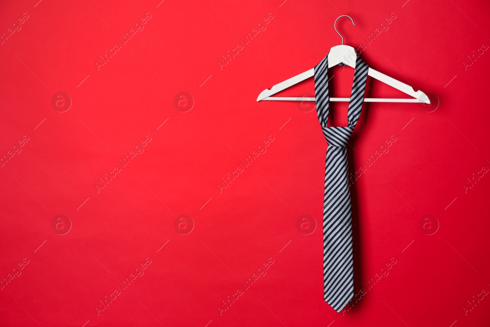 Photo of Hanger with striped tie on red background. Space for text