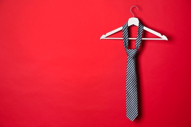 Photo of Hanger with striped tie on red background. Space for text