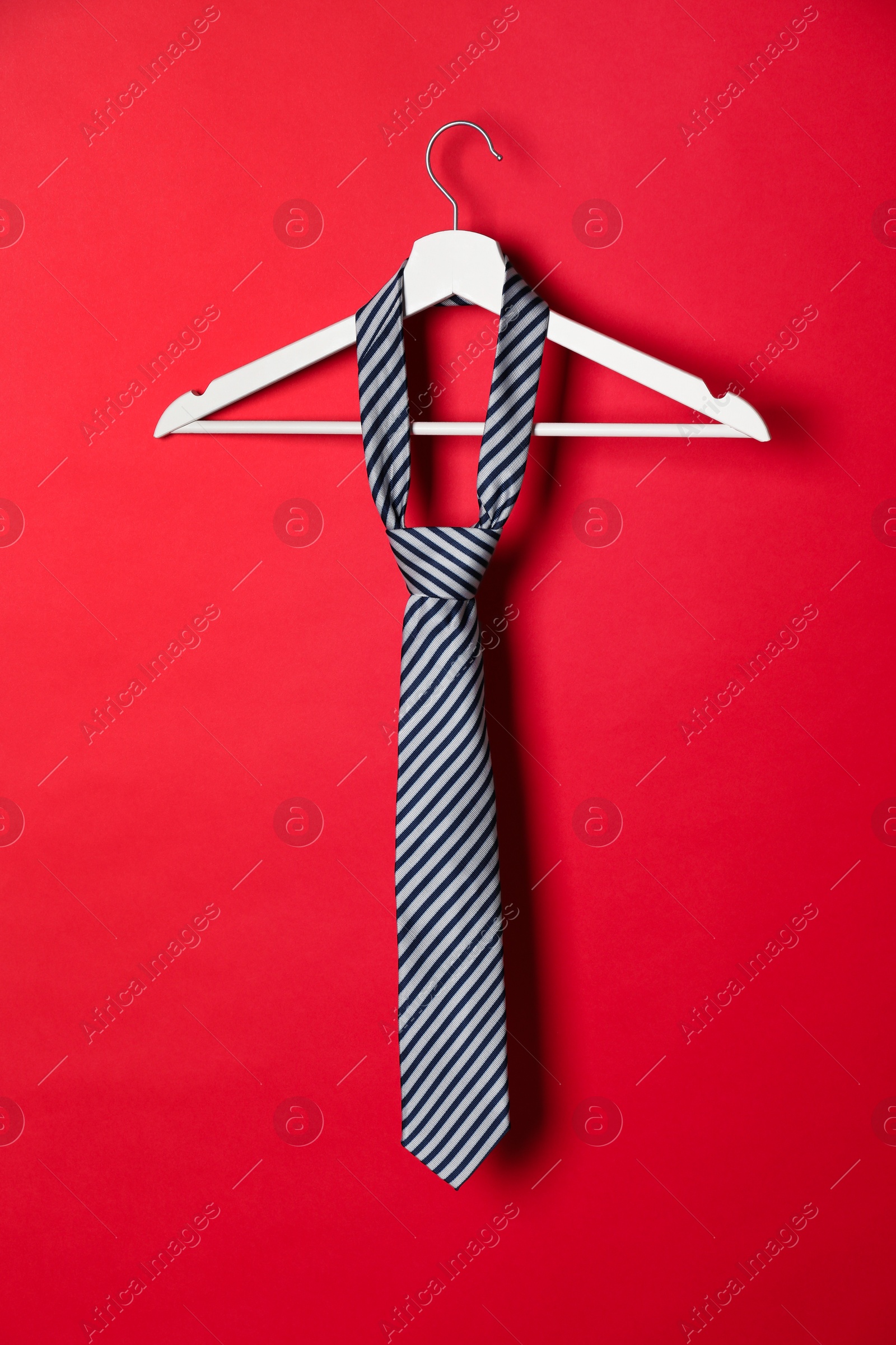Photo of Hanger with striped tie on red background