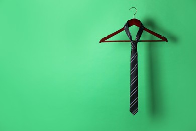Photo of Hanger with black striped tie on green background. Space for text