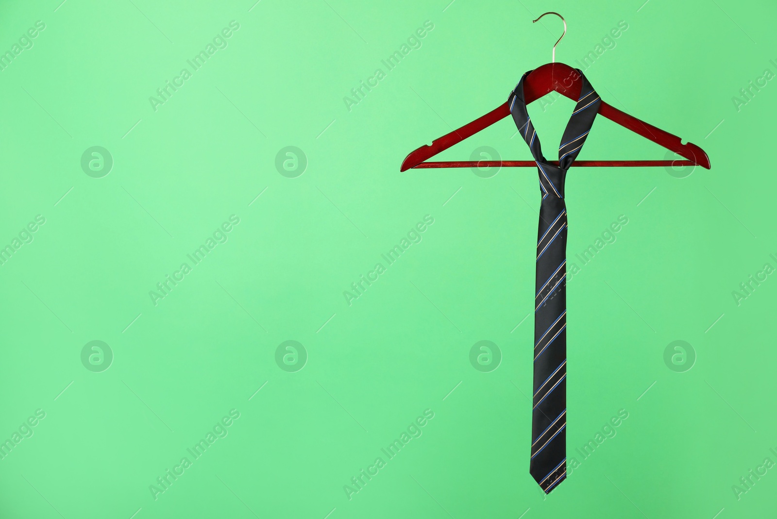 Photo of Hanger with black striped tie on green background. Space for text