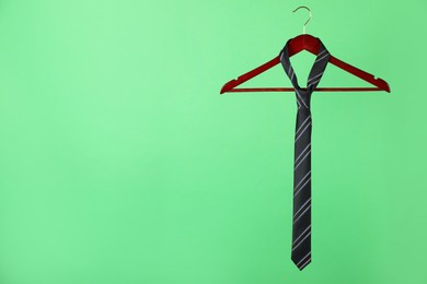 Hanger with black striped tie on green background. Space for text