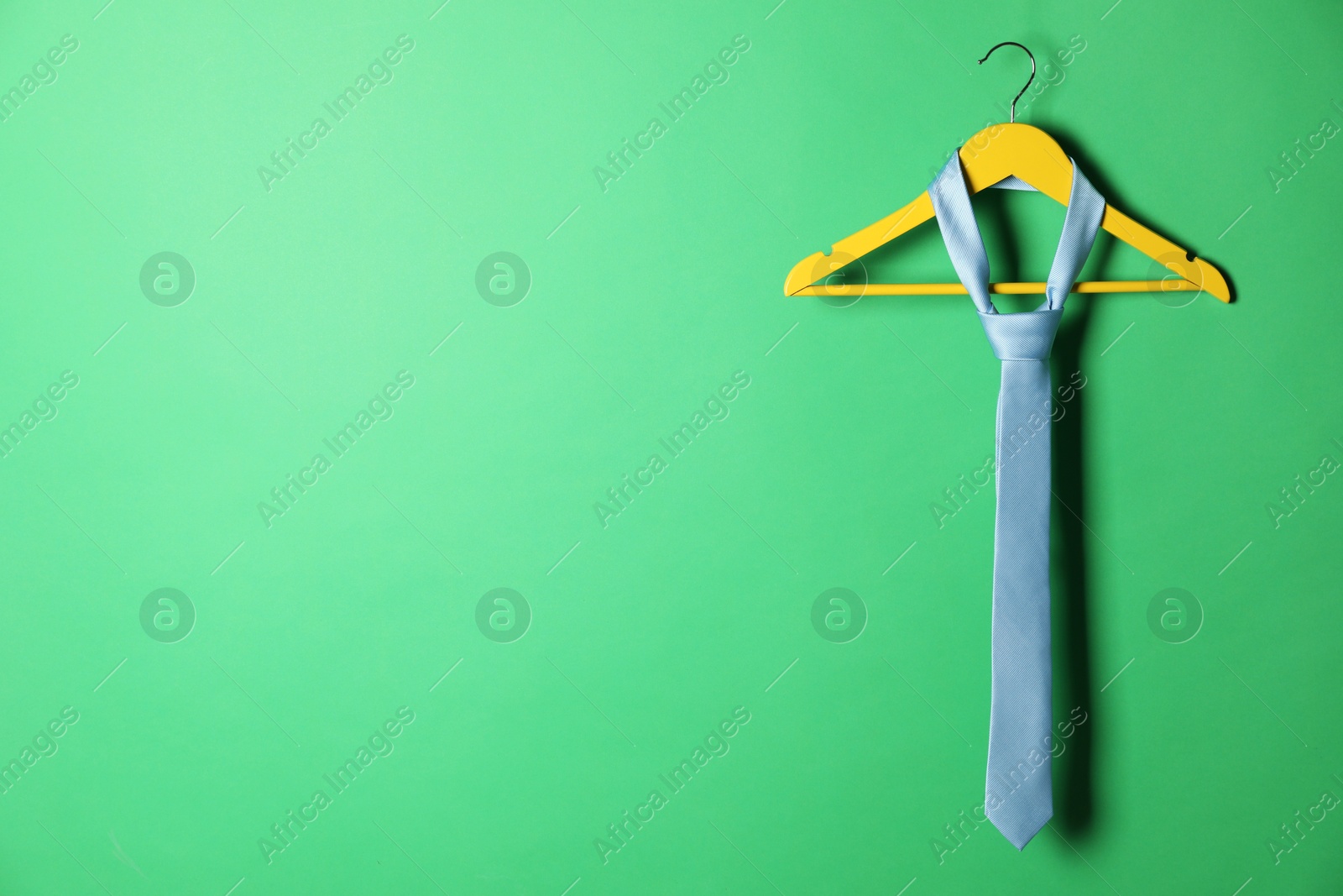 Photo of Hanger with light blue tie on green background. Space for text