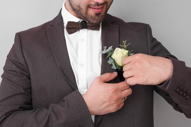 Groom with boutonniere on light grey background, closeup. Wedding accessory