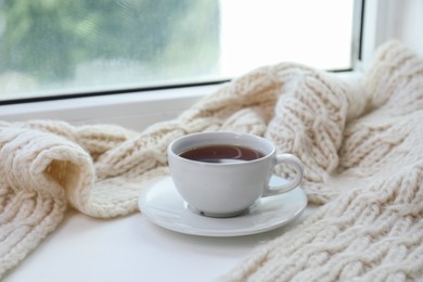 Beige knitted scarf and tea on windowsill