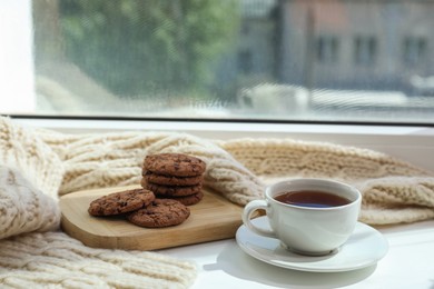 Beige knitted scarf, tea and cookies on windowsill