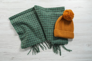 Soft green scarf and knitted hat on white wooden table, top view