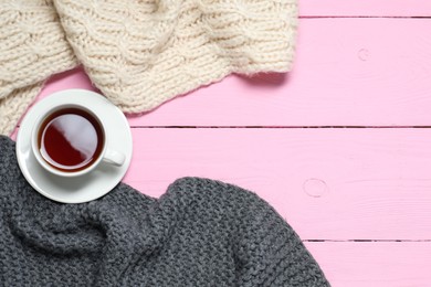 Photo of Knitted scarfs and tea on pink wooden table, flat lay. Space for text