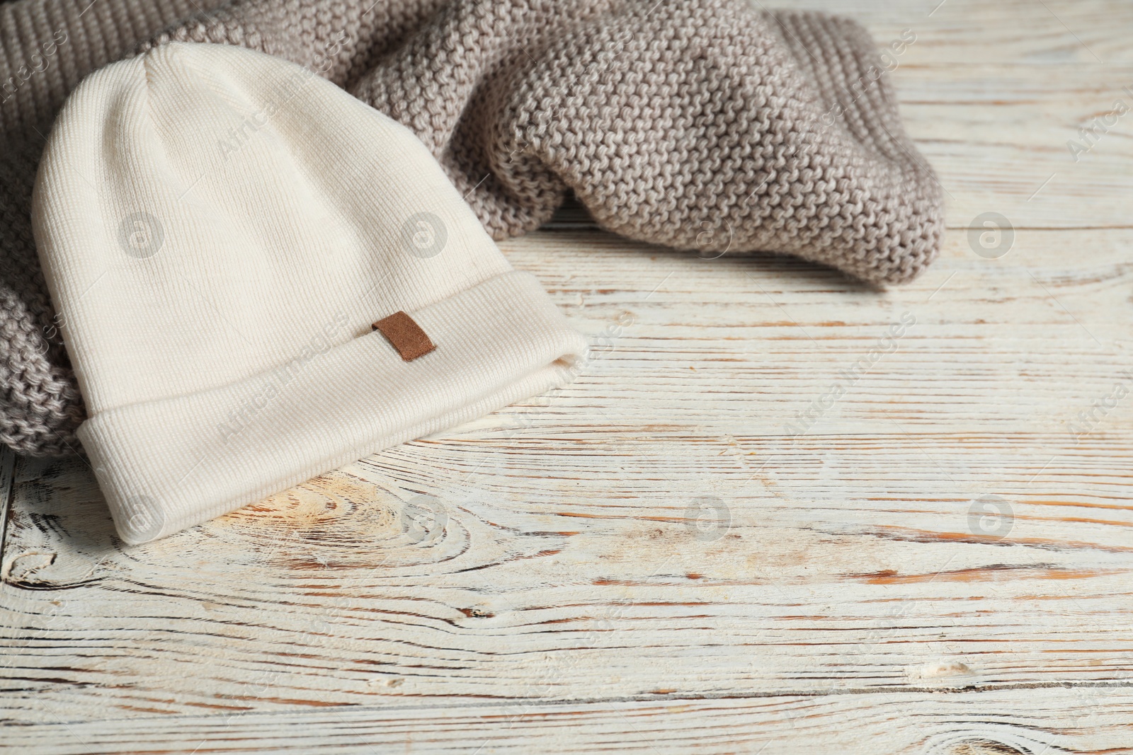 Photo of Gray knitted scarf and hat on wooden table, space for text