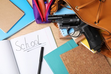Photo of Gun and school stationery on wooden table, flat lay