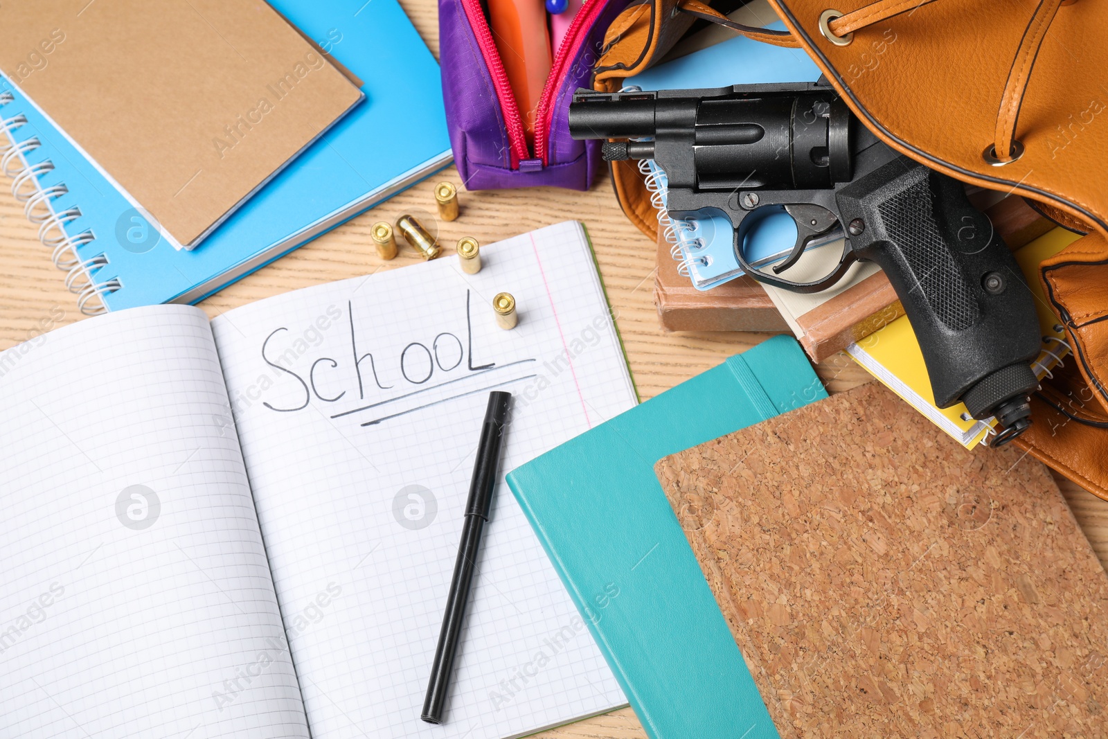 Photo of Gun, bullets and school stationery on wooden table, flat lay