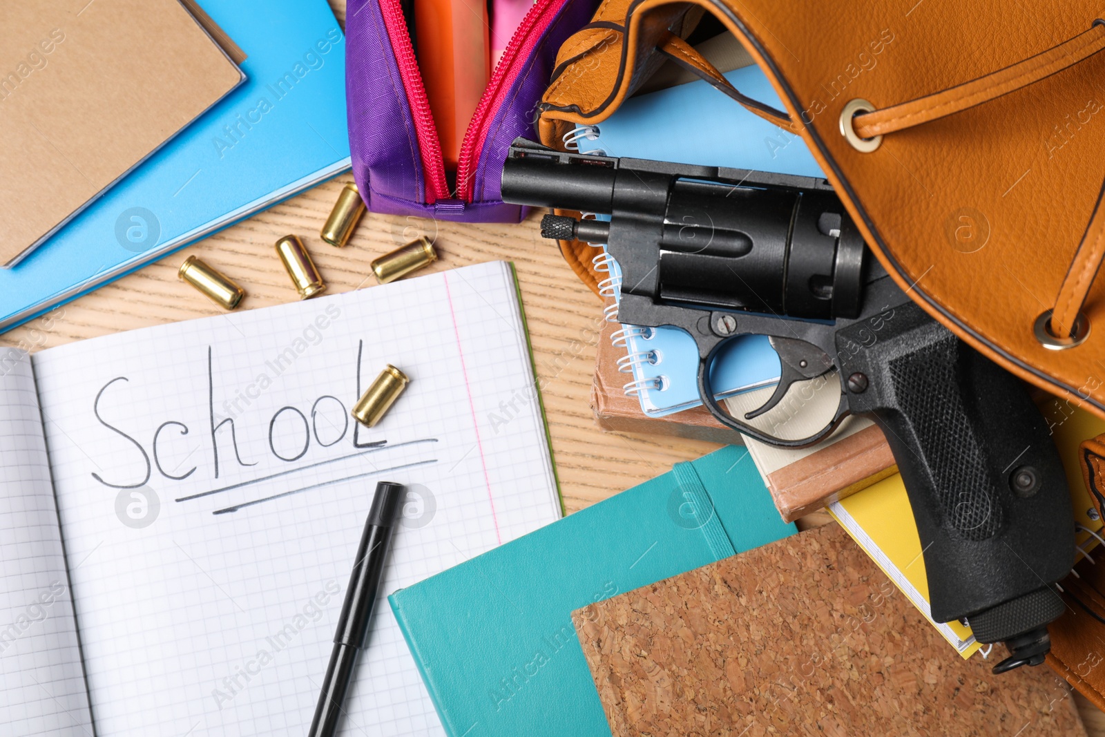 Photo of Gun, bullets and school stationery on wooden table, flat lay