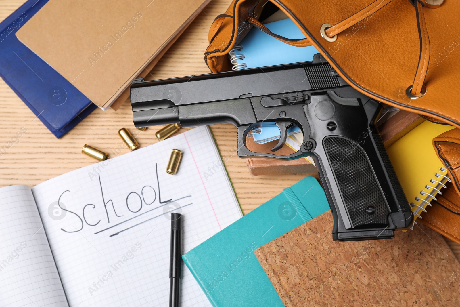 Photo of Gun, bullets and school stationery on wooden table, flat lay