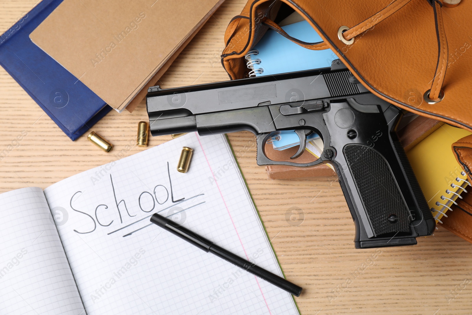 Photo of Gun, bullets and school stationery on wooden table, flat lay