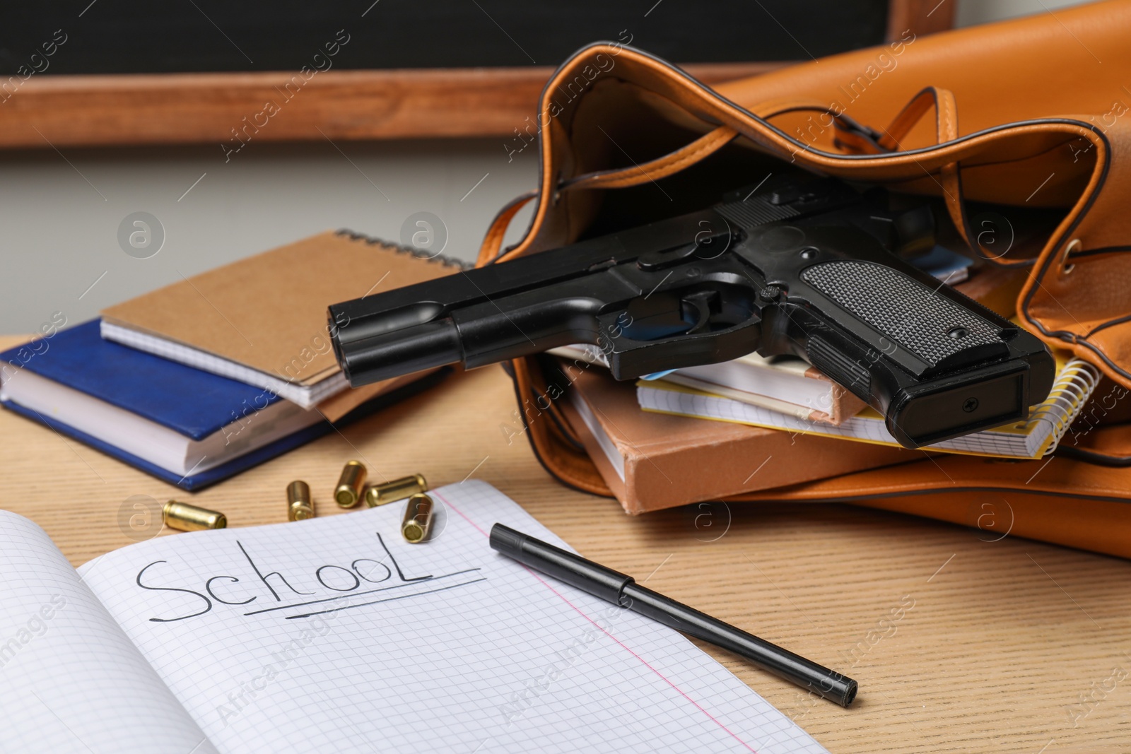 Photo of Gun, bullets and school stationery on wooden table