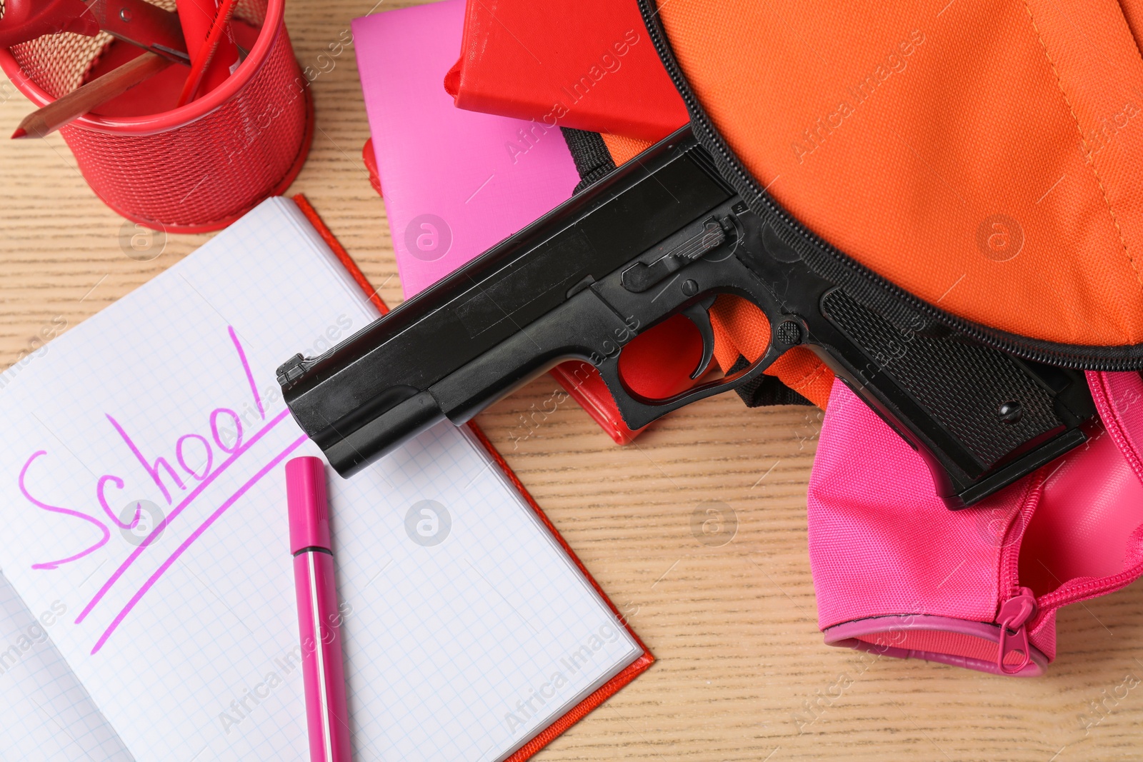 Photo of Gun and school stationery on wooden table, flat lay