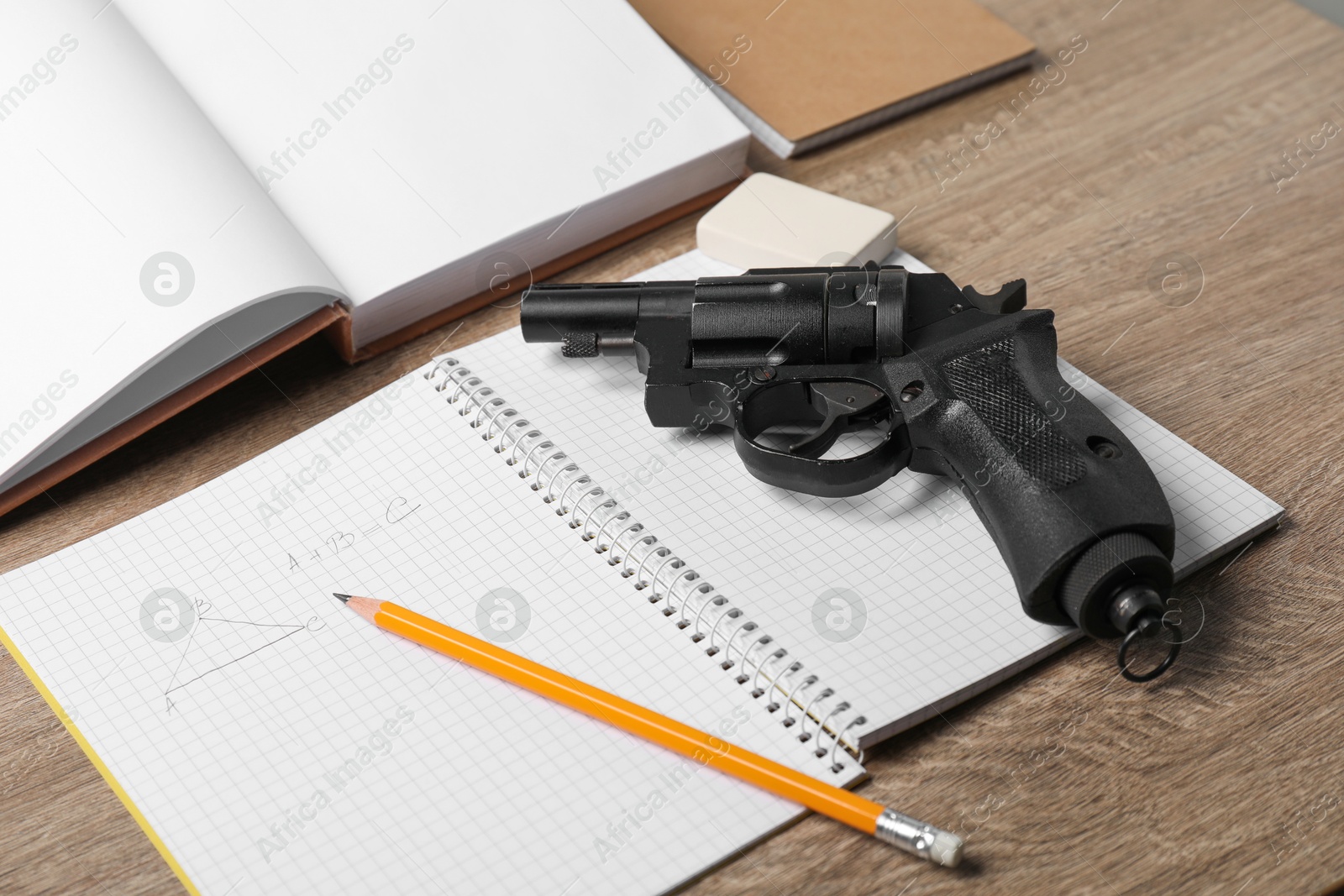 Photo of Gun and school stationery on wooden table, closeup