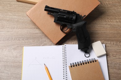 Photo of Gun and school stationery on wooden table, flat lay
