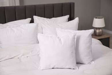 Photo of Many soft white pillows and duvet on bed indoors