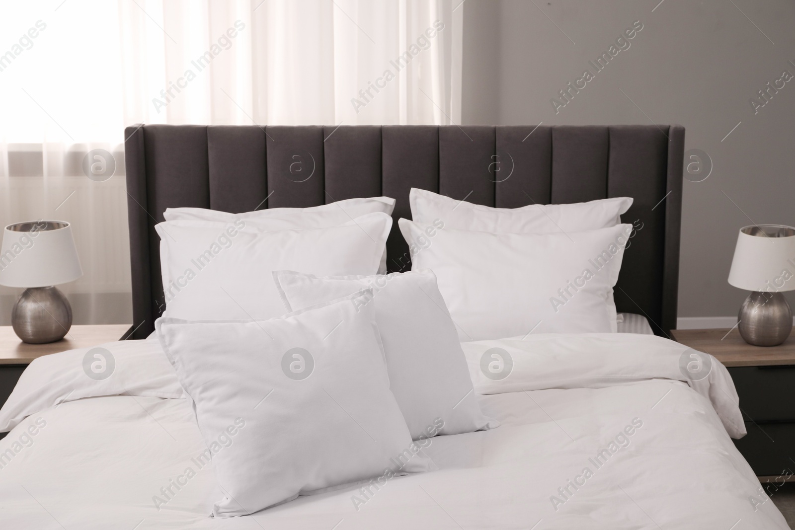 Photo of Many soft white pillows and duvet on bed indoors